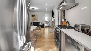 Eine moderne Küche mit Edelstahlgeräten, ein Essbereich mit Sofa und Couchtisch sowie ein Flur, der in ein Wohnzimmer führt.