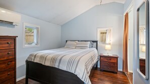 Un dormitorio con cama, cómoda, mesita de noche, ventilador de techo y ventana.
