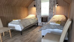 A cozy attic bedroom with two single beds, wooden flooring, and a small TV. - Åtte Årstider Lodge (South Varanger)