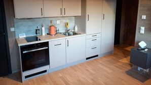 A modern kitchen with white cabinets, a built-in oven, and a countertop with various appliances and utensils. - Åtte Årstider Lodge (South Varanger)