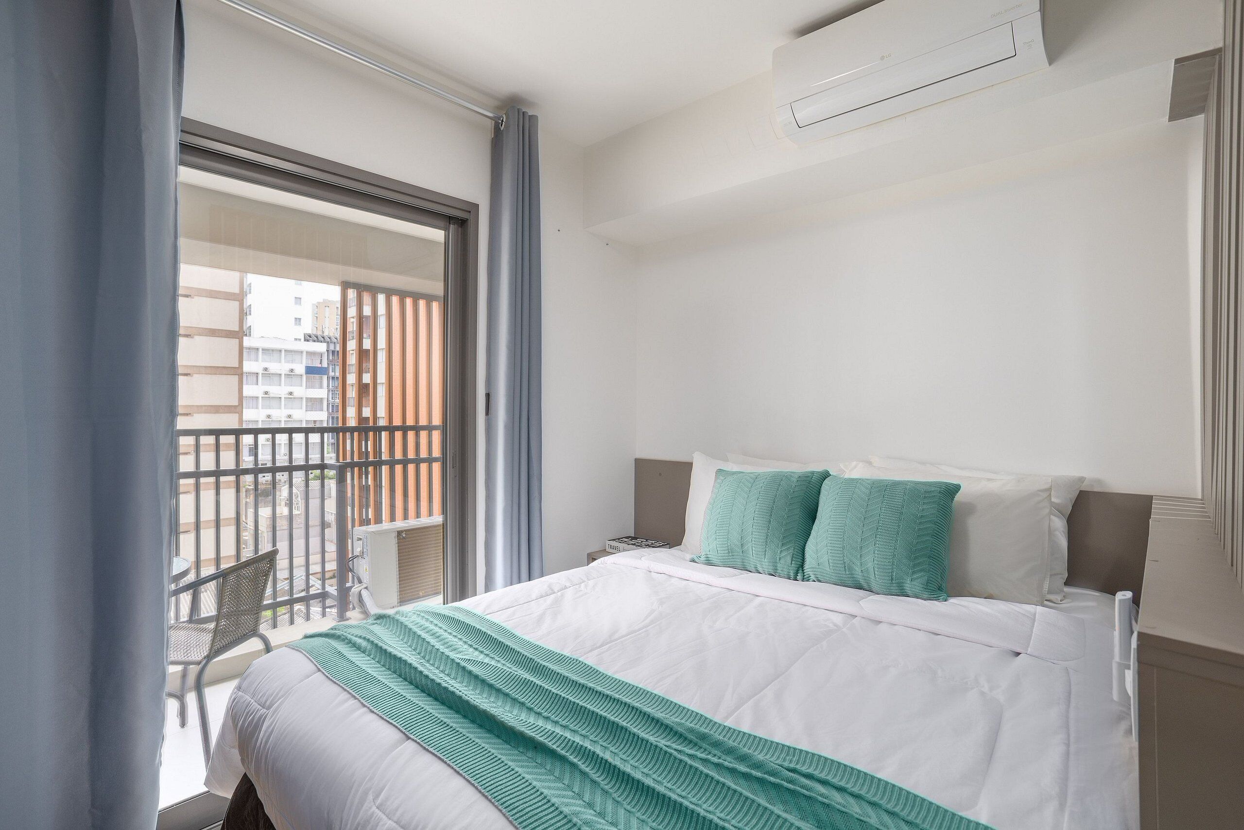 A hotel room with a bed, a nightstand, a window with curtains, and a view of the outside balcony.