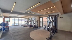 Ein modernes Fitnessstudio mit Laufbändern, Crosstrainern und Gewichteinrichtungen. Große Fenster sorgen für natürliches Licht und einen Ausblick nach draußen.