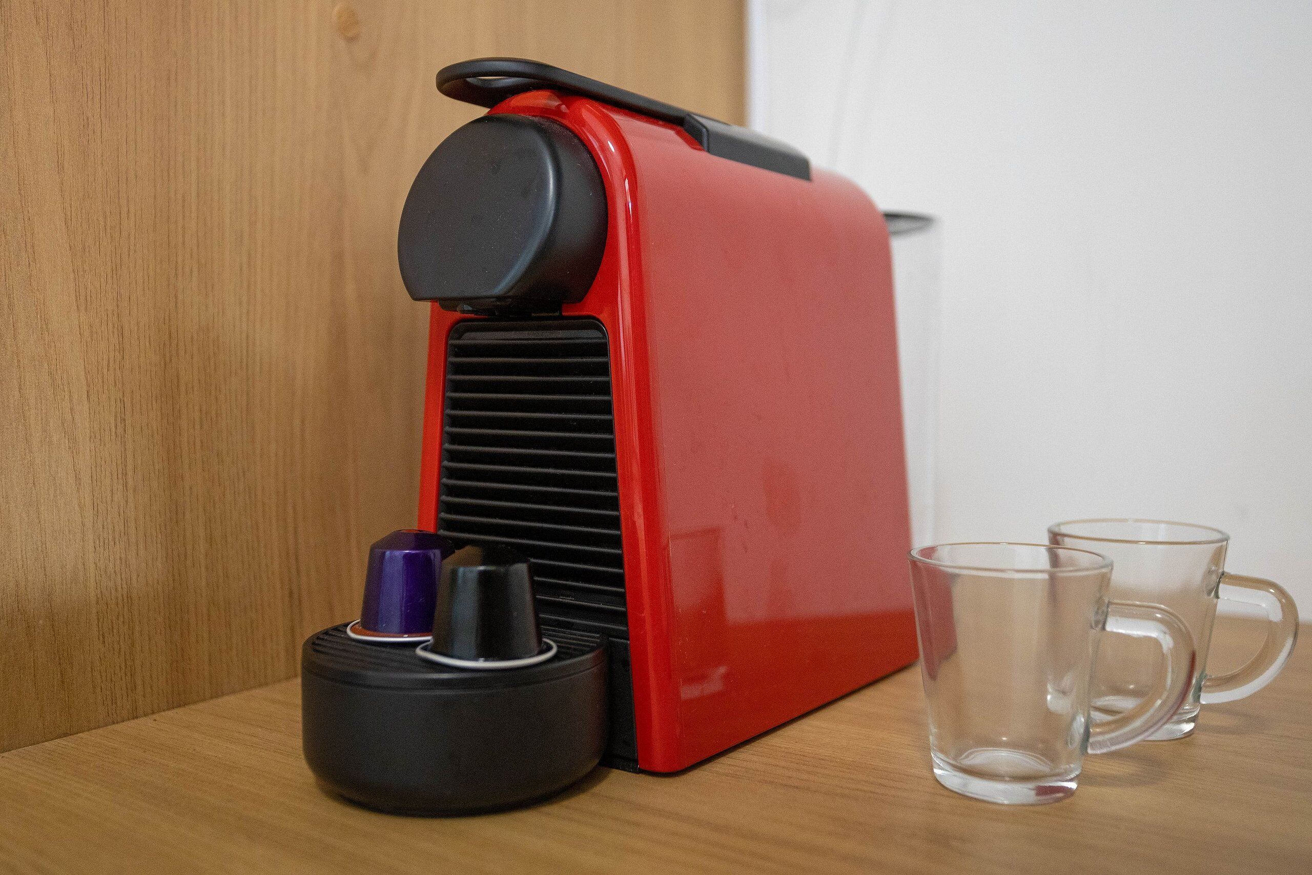 Une machine à café rouge, avec deux tasses en verre transparent posées sur une surface en bois.
