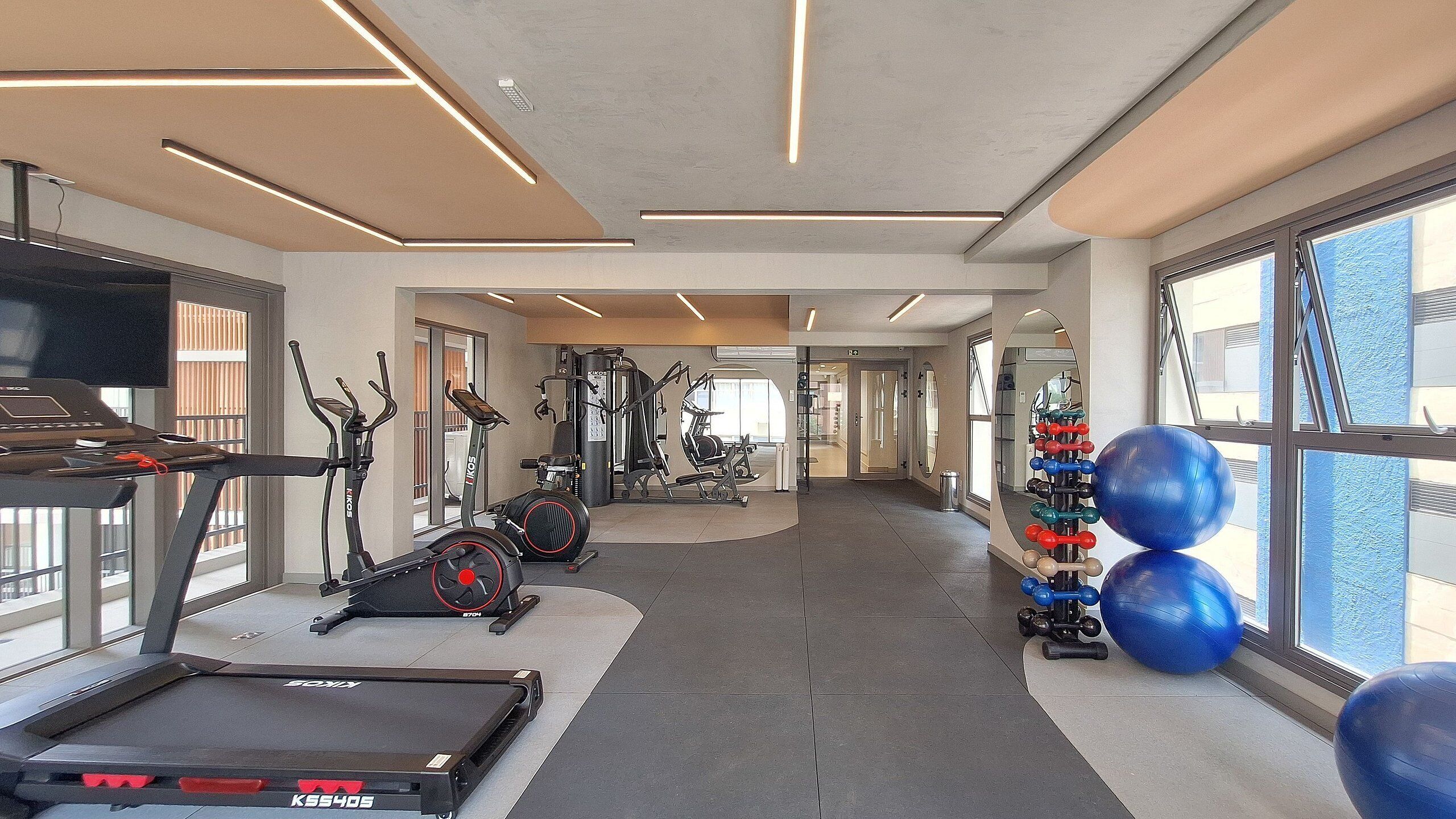 Un gimnasio moderno con equipo de cardio, máquinas de pesas y pelotas de ejercicio.