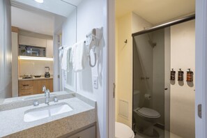 A bathroom with a sink, a toilet, a shower, and a hairdryer mounted on the wall. - H.Paulista (São Paulo)