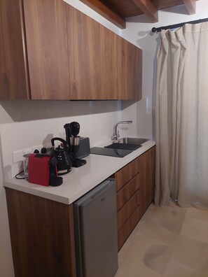 A compact kitchen with wooden cabinets, a built-in dishwasher, a coffee maker, and a kettle.