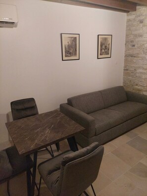 A room with a sofa, a dining table with chairs, and two framed pictures on the wall.