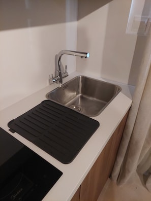 A modern kitchen with a stainless steel sink, a black cutting board, and a built-in induction cooktop.