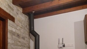 A room with a stone wall, a black wood-burning stove, a chair, and a power outlet on the wall.