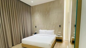 A modern hotel room with a large bed, wooden flooring, and a large mirror. - Baithans Furnished Apartments (Ajman)