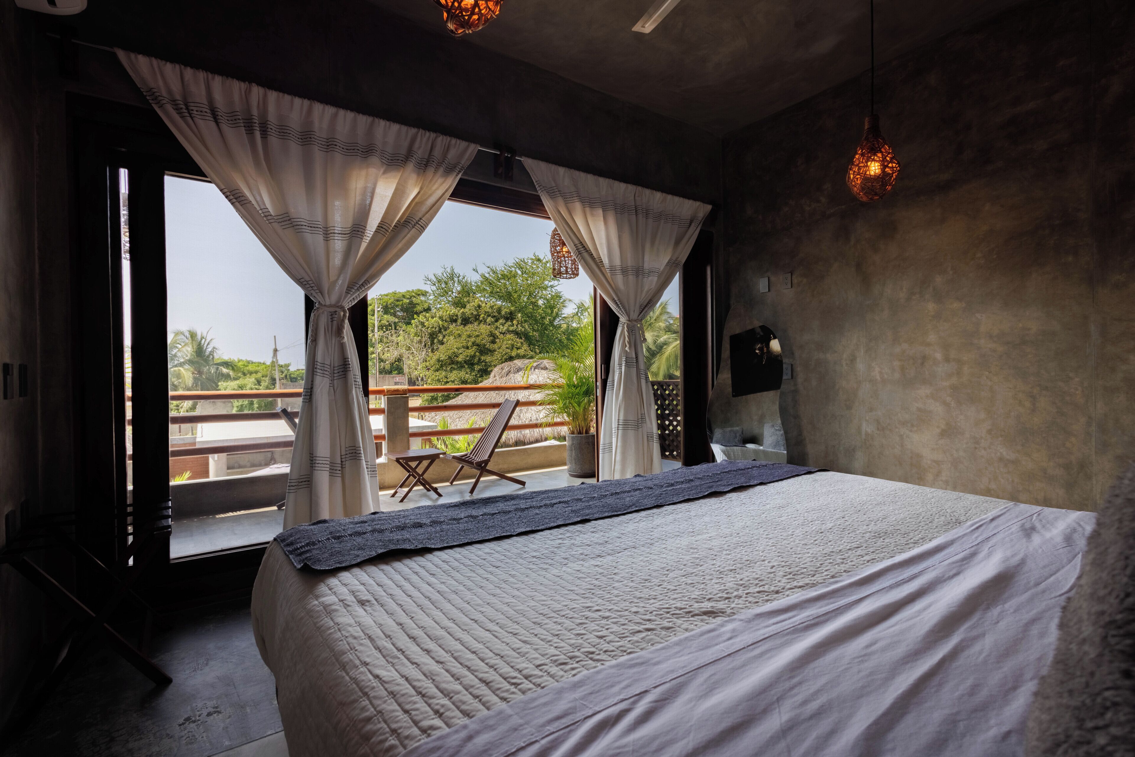 Un dormitorio con una cama grande, un balcón con una silla y cortinas.