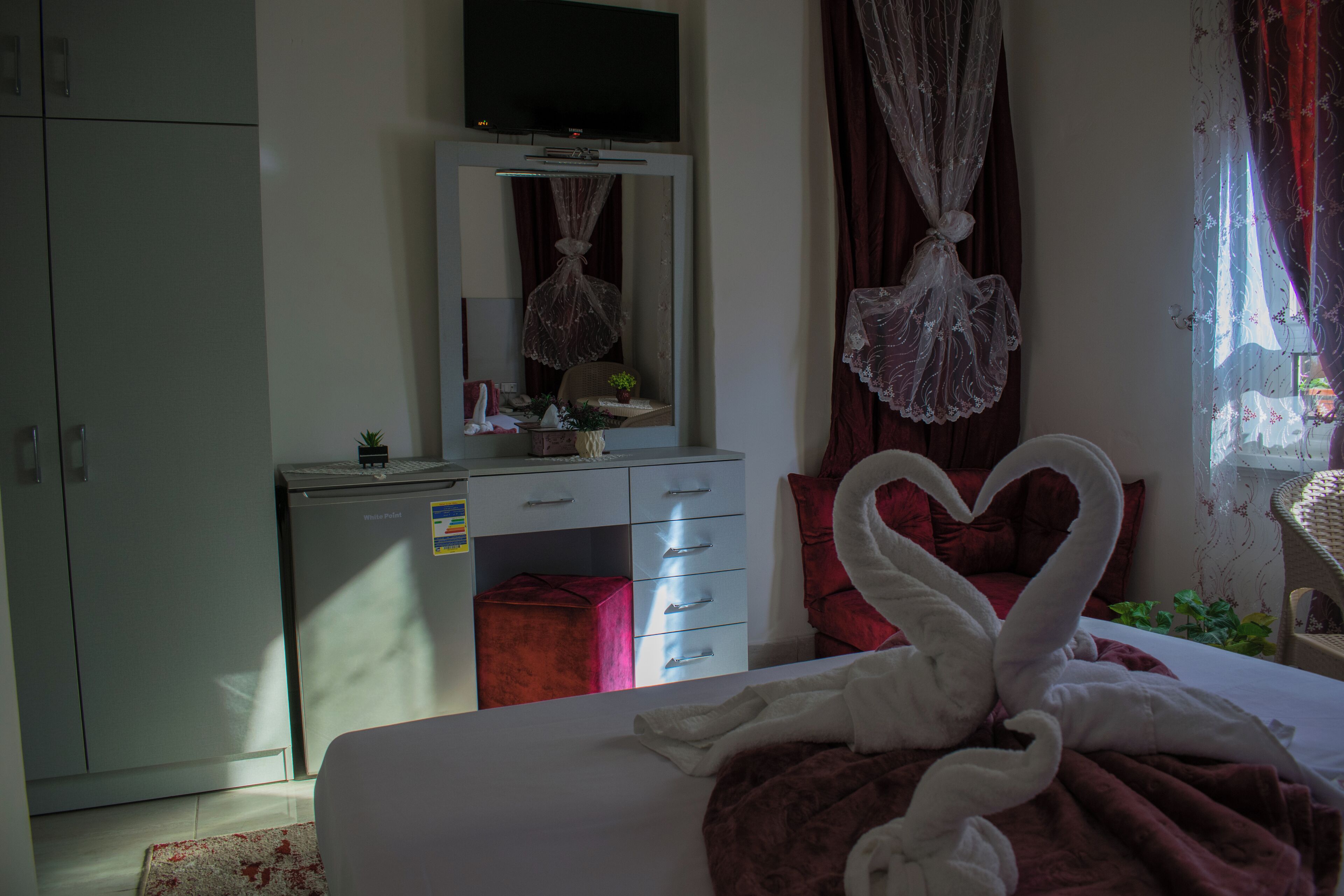 Una camera da letto con un letto, una cassettiera, una televisione e una finestra con tende.
