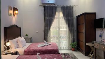 Habitación de hotel con dos camas, un escritorio, un televisor y un ventanal con cortinas.