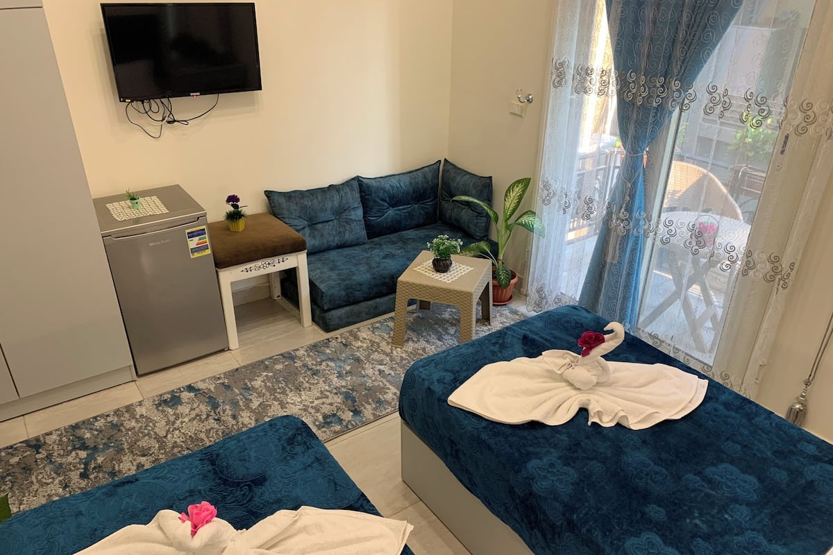 A hotel room with two beds, a sofa, a small table, a refrigerator, and a TV on the wall.