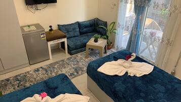 Habitación de hotel con dos camas, un sofá, una mesita, un refrigerador y un televisor en la pared.