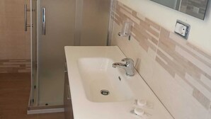 Un baño con ducha envuelta en cristal, un lavabo blanco con espejo y un perchero para toallas.