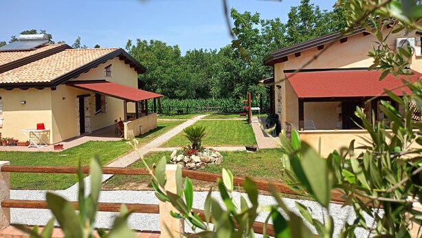 Zona residencial con dos casas, ambas con techo rojo y paredes color beige, rodeadas de follaje y un cielo despejado.