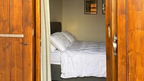 Una puerta de madera que da paso a un dormitorio con una cama, aire acondicionado de pared y cuadros enmarcados.