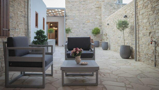 A courtyard with stone walls, two grey sofas, a table with a vase of flowers, and potted plants.