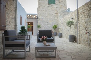 Un patio con muros de piedra, dos sofás grises, una mesa con un jarrón de flores y plantas en macetas.