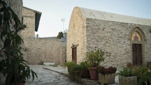 A stone building with a curved roof, a small arched window with a religious icon, and potted plants in the foreground.