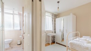 A hospital room with a bed, a bedside table, a window with curtains, a white wardrobe, and a toilet. - Quaint 1BD Flat with Balcony in Maida Vale (Greater London)