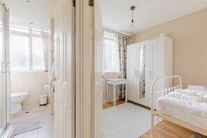 A hospital room with a bed, a bedside table, a window with curtains, a white wardrobe, and a toilet. - Quaint 1BD Flat with Balcony in Maida Vale (Greater London)