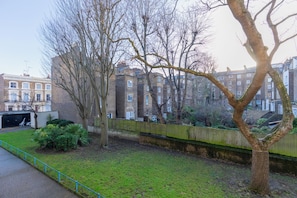 A residential area with a tree-lined street, brick buildings, and a fence. - Quaint 1BD Flat with Balcony in Maida Vale (Greater London)