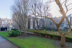 A residential area with a tree-lined street, brick buildings, and a fenced yard. - Quaint 1BD Flat with Balcony in Maida Vale (Greater London)