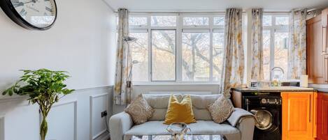 A living room with a sofa, a coffee table, a potted plant, and a clock on the wall.