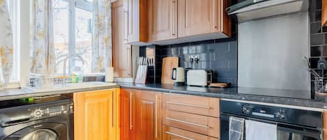 Une cuisine avec des meubles de rangement en bois, un lave-linge, un grille-pain et un lave-vaisselle.