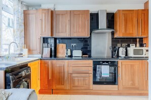 Una cocina moderna con armarios de madera, campana extractora de acero inoxidable, lavavajillas, microondas y tostadora.