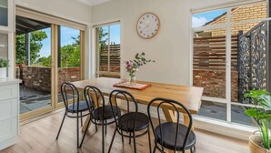 Uma sala de jantar com uma mesa de madeira, quatro cadeiras pretas, um relógio e um vaso de flores.
