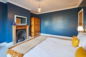 A bedroom with a large bed, a wooden wardrobe, a fireplace, and a mirror.