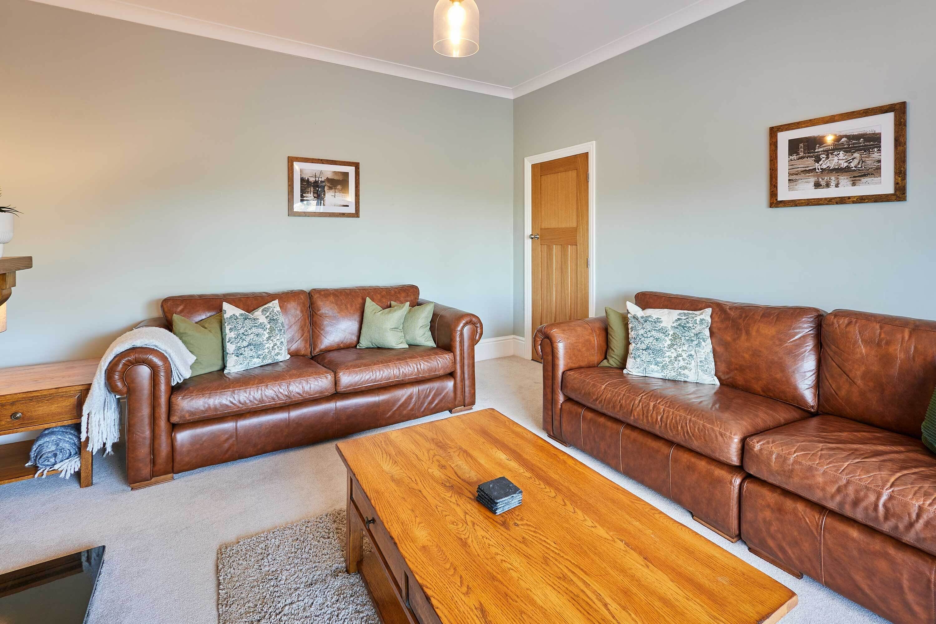 A living room with two brown leather sofas, a wooden coffee table, and a door leading to another room.