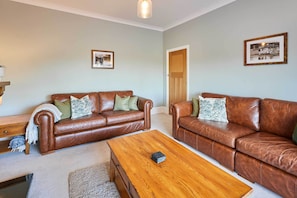 A living room with two brown leather sofas, a wooden coffee table, and a door leading to another room.