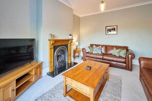 A living room with a TV, fireplace, leather sofa, coffee table, and a framed picture on the wall.