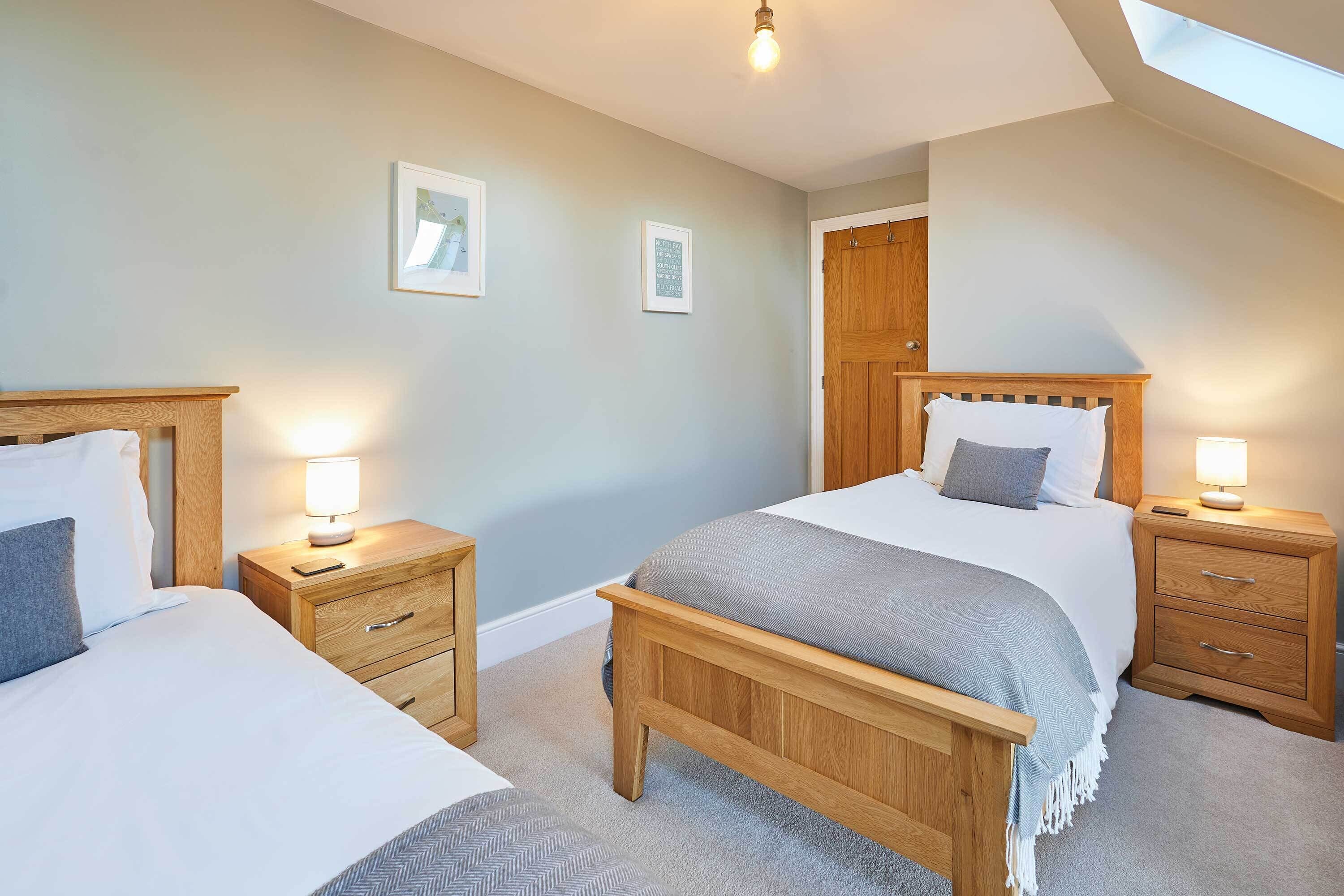 A bedroom with two beds, wooden headboards, bedside tables with lamps, and a skylight.