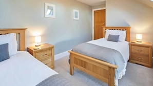 A bedroom with two beds, wooden headboards, bedside tables with lamps, and a skylight.