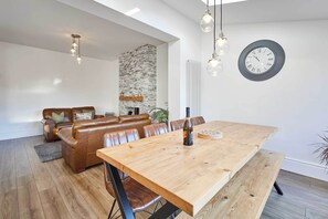 A modern living room with a wooden dining table, leather sofas, and a stone accent wall.