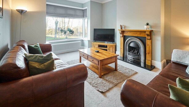 A living room with a sofa, coffee table, TV, fireplace, and a view of the outdoors.