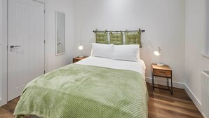 Une chambre à coucher comprenant un lit, deux tables de chevet, une commode, un miroir et une porte.