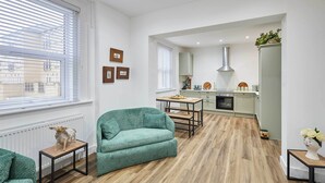 Un salon moderne avec un canapé vert, une table à manger et une cuisine en arrière-plan.