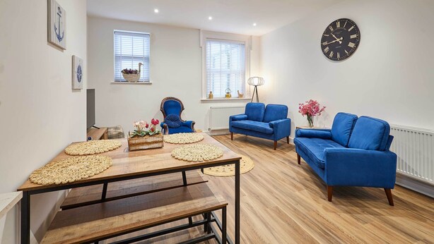 Una sala de estar moderna con una mesa de madera, sofás azules y un reloj de pared grande.