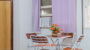 A dining area with a table and four chairs, a vase with flowers, and a window with curtains.