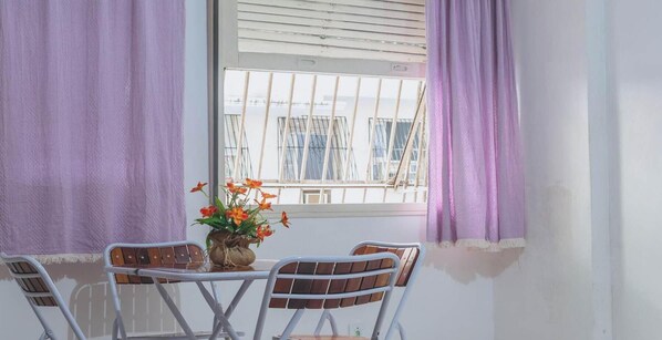Ein Zimmer mit Fenster, einem Tisch mit Stühlen und einer Blumenvase.