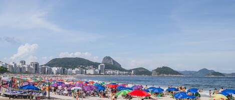A beach with umbrellas and people, a cityscape with buildings, and a mountain in the background.
