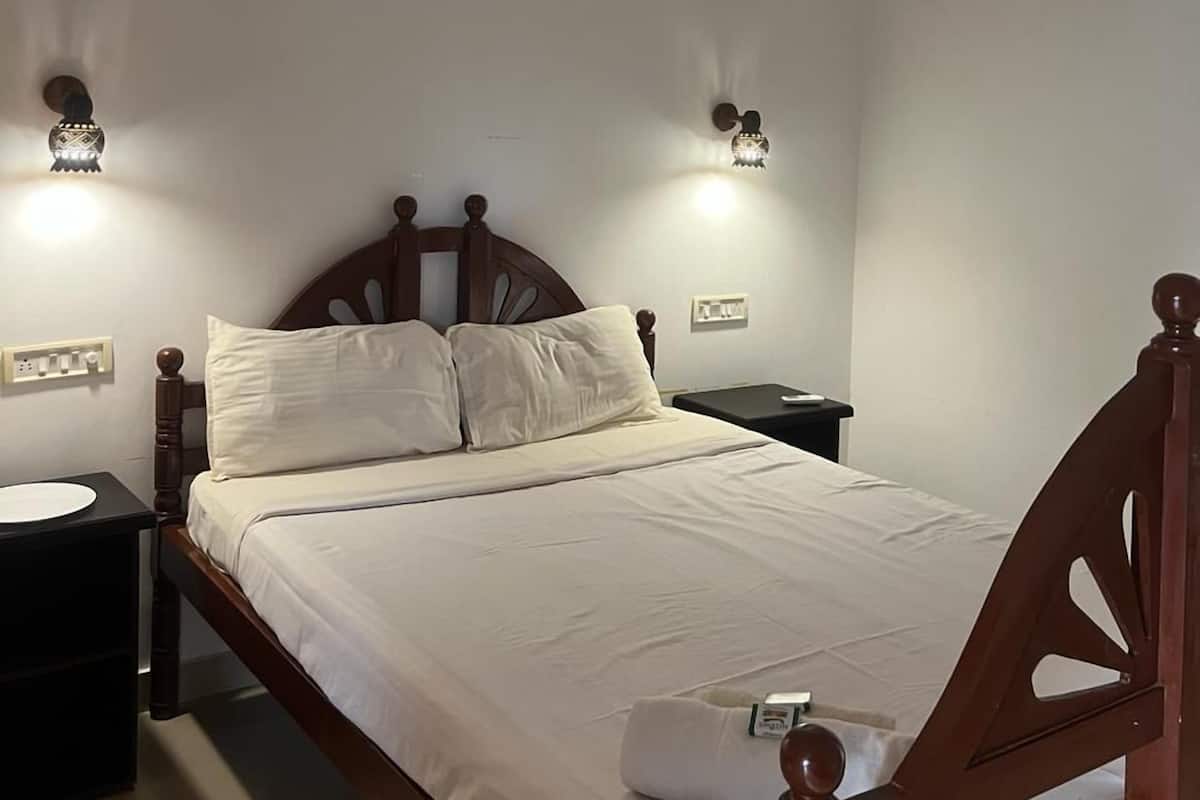 A neatly made bed in a room with a wooden headboard, two bedside tables, and wall-mounted light fixtures.