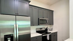 A modern kitchen with stainless steel appliances, grey cabinets, and a white countertop.