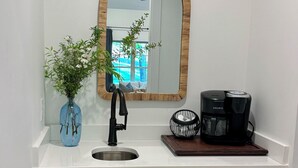 A kitchen with a sink, a mirror, a coffee maker, and a plant.